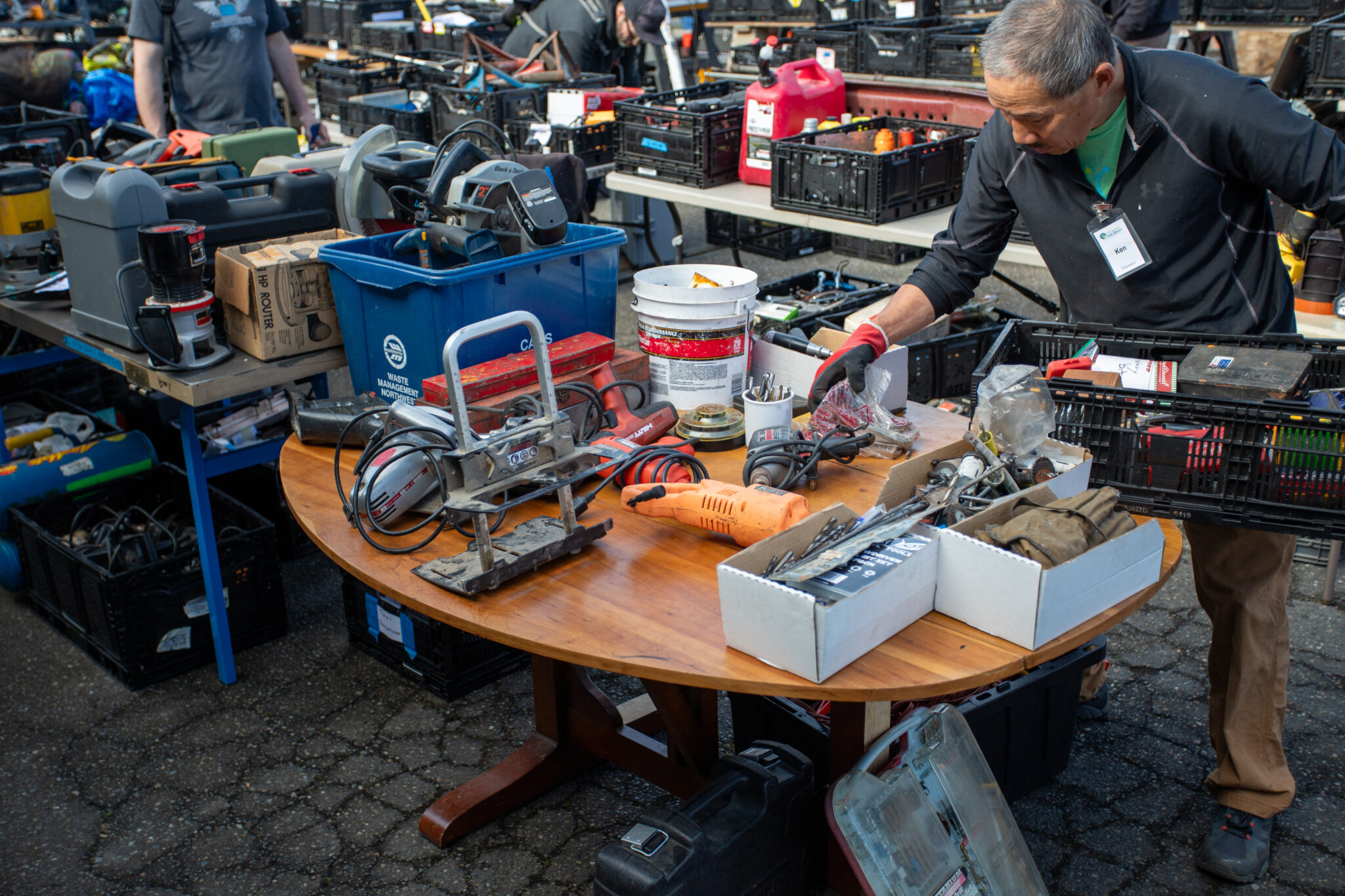 An individual holding some tools while taking a look at the abundance of tools on the table at the Shoreline Tool Sale. There are plenty of tools organized on tables all around them.