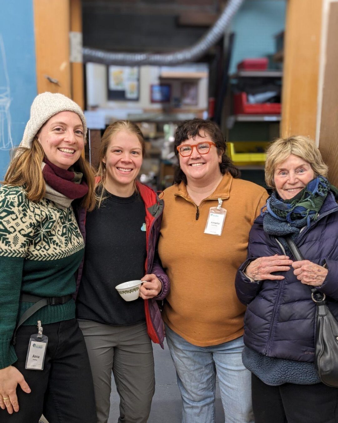 Four staff, volunteers, and community members are standing in the Workshop of the NE Seattle Tool Library during the open house to celebrate 12 years of tool lending.