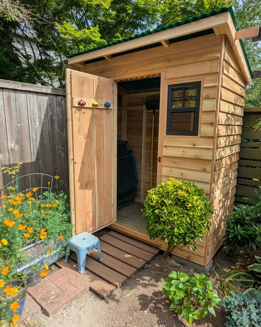 The door of James' wooden, backyard shed is propped open to reveal umbrella hooks and a small space for storing items.