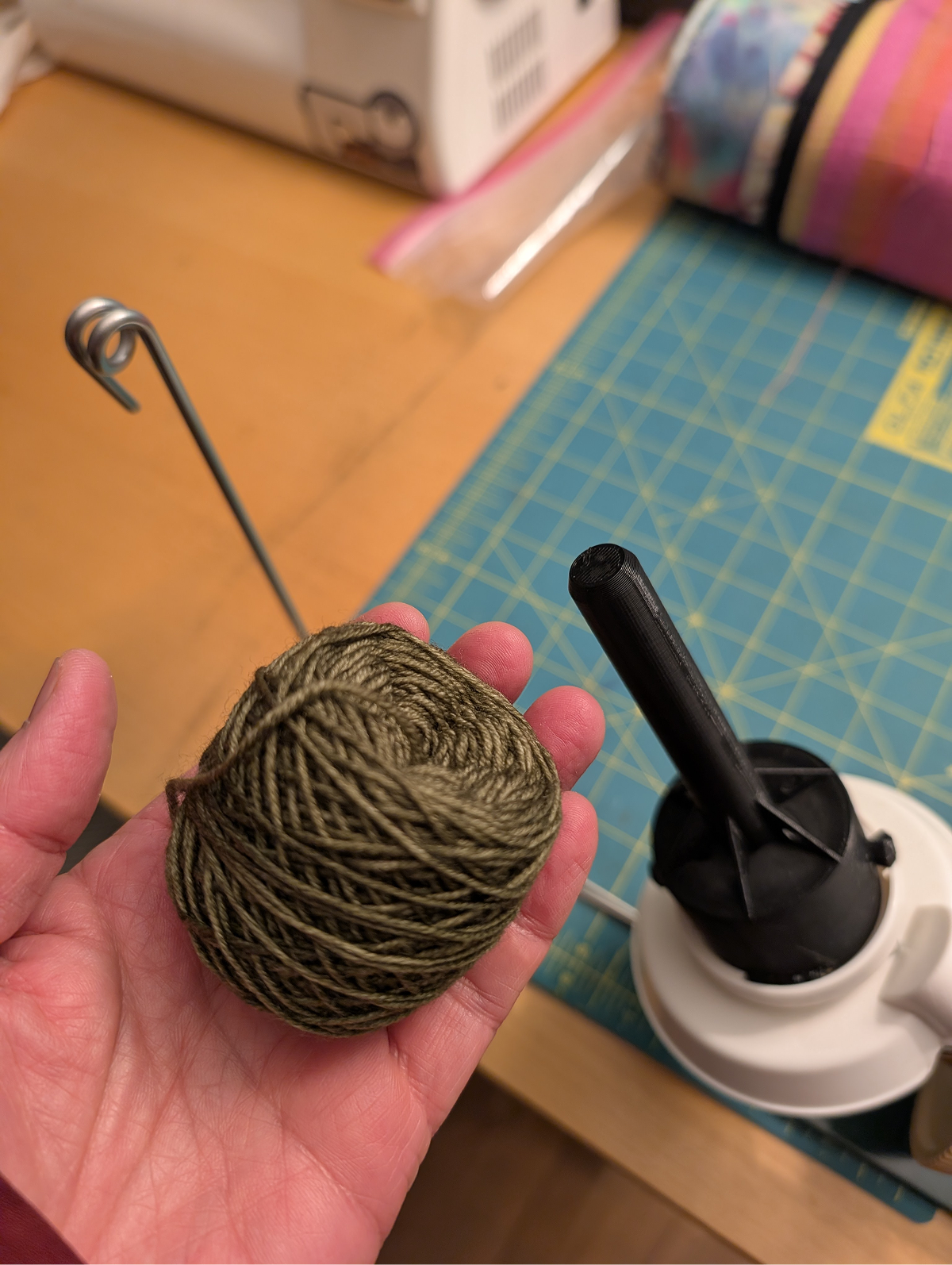 A hand holds a small skein of yarn that was created with the 3D printed yarn winder adaptor in the background.