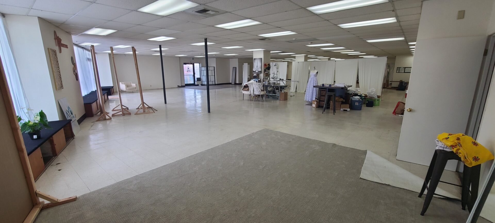 There are random tables, art supplies, poles, and other things throughout an empty office space.