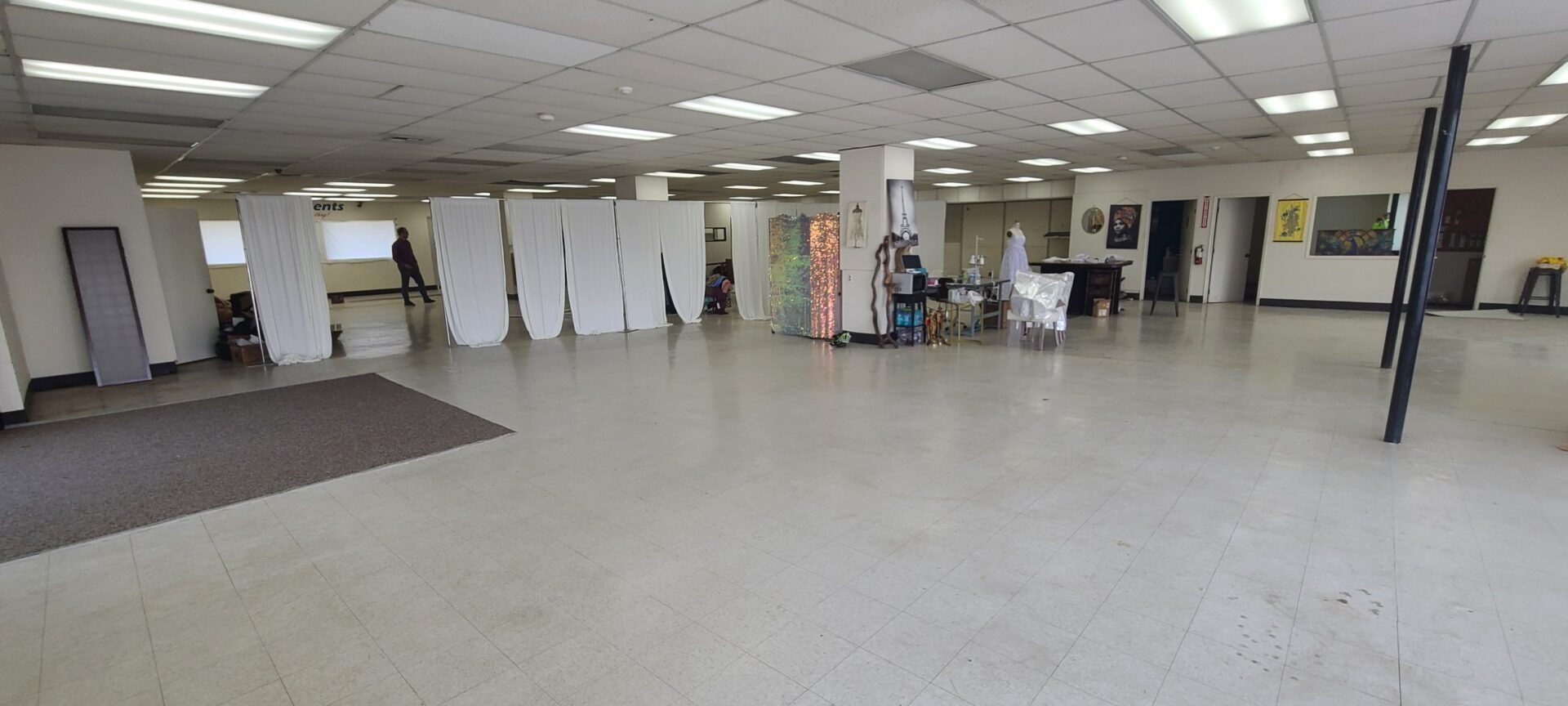 A mostly empty space within a building. There are some sheets hanging up, along with different pieces of art near the center of the room.