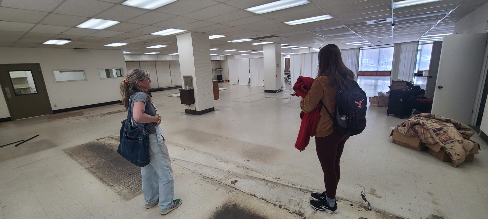 Two people look at a large empty office space in front of them.