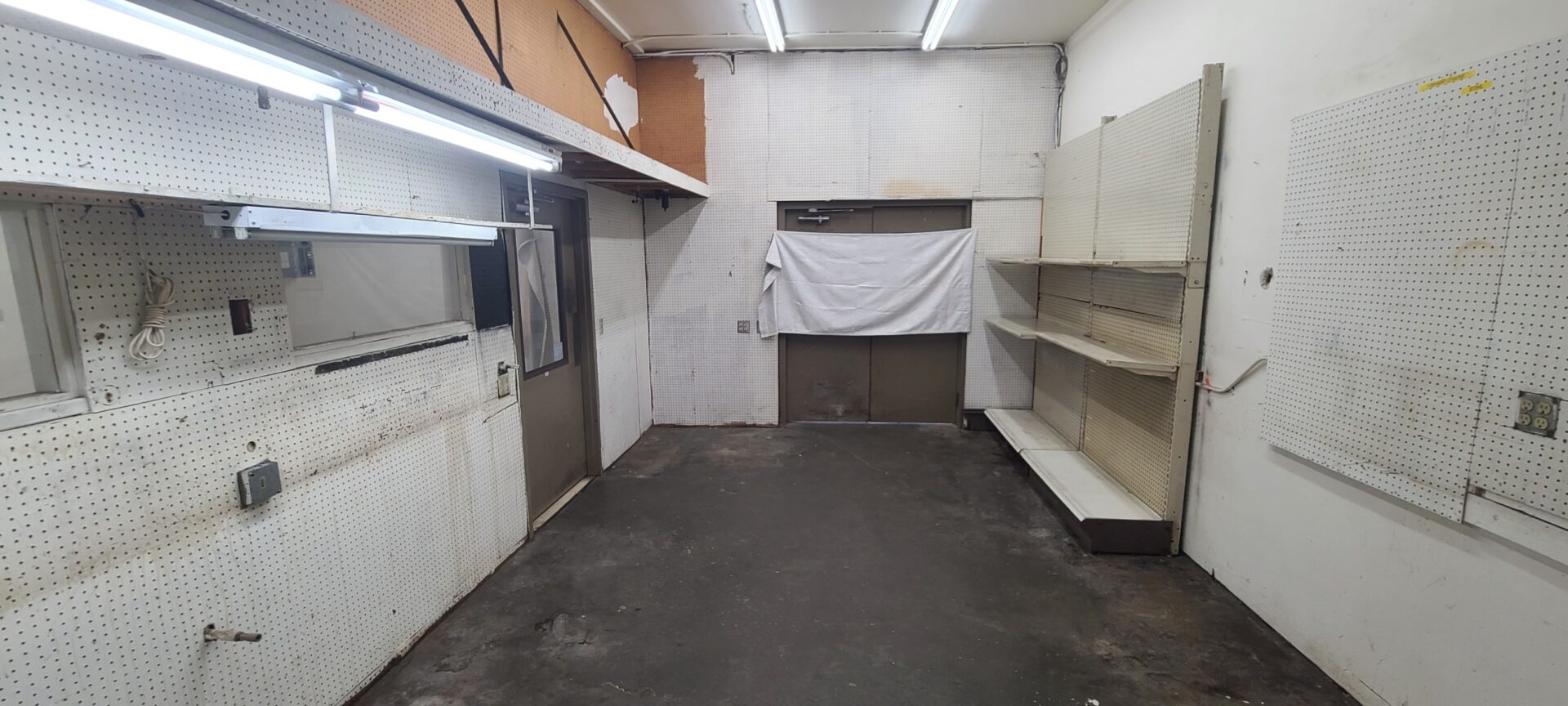 A small room with pegboard walls and empty shelving.