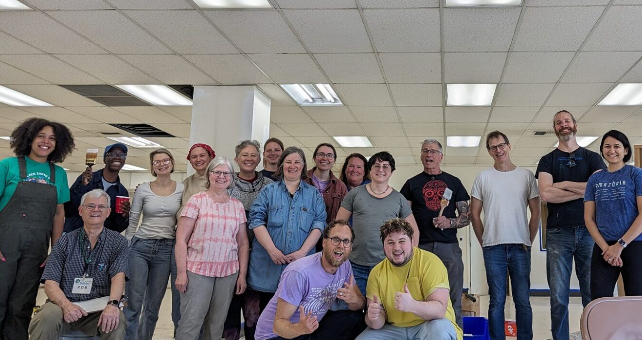 A group of volunteers and staff smile in a white, mostly empty building that they plan to paint and clean up. It will become the new Reuse Commons Lake City space.