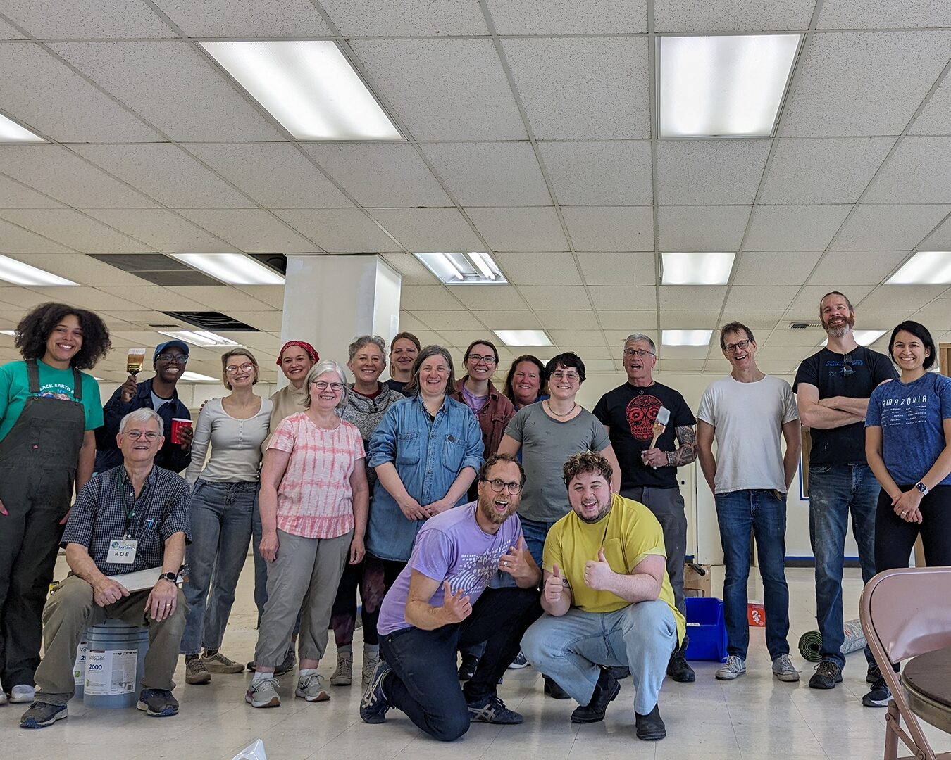 A group of volunteers and staff smile in a white, mostly empty building that they plan to paint and clean up. It will become the new Reuse Commons Lake City space.